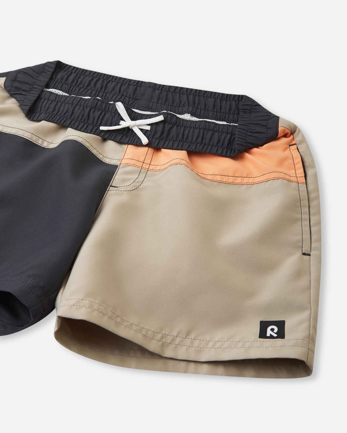 Close-up detail of the Reima Palmu kids' soft black color block swim shorts, showcasing the adjustable white drawstring waist for a custom fit, neat stitching, and the signature Reima logo tag on the hem.
