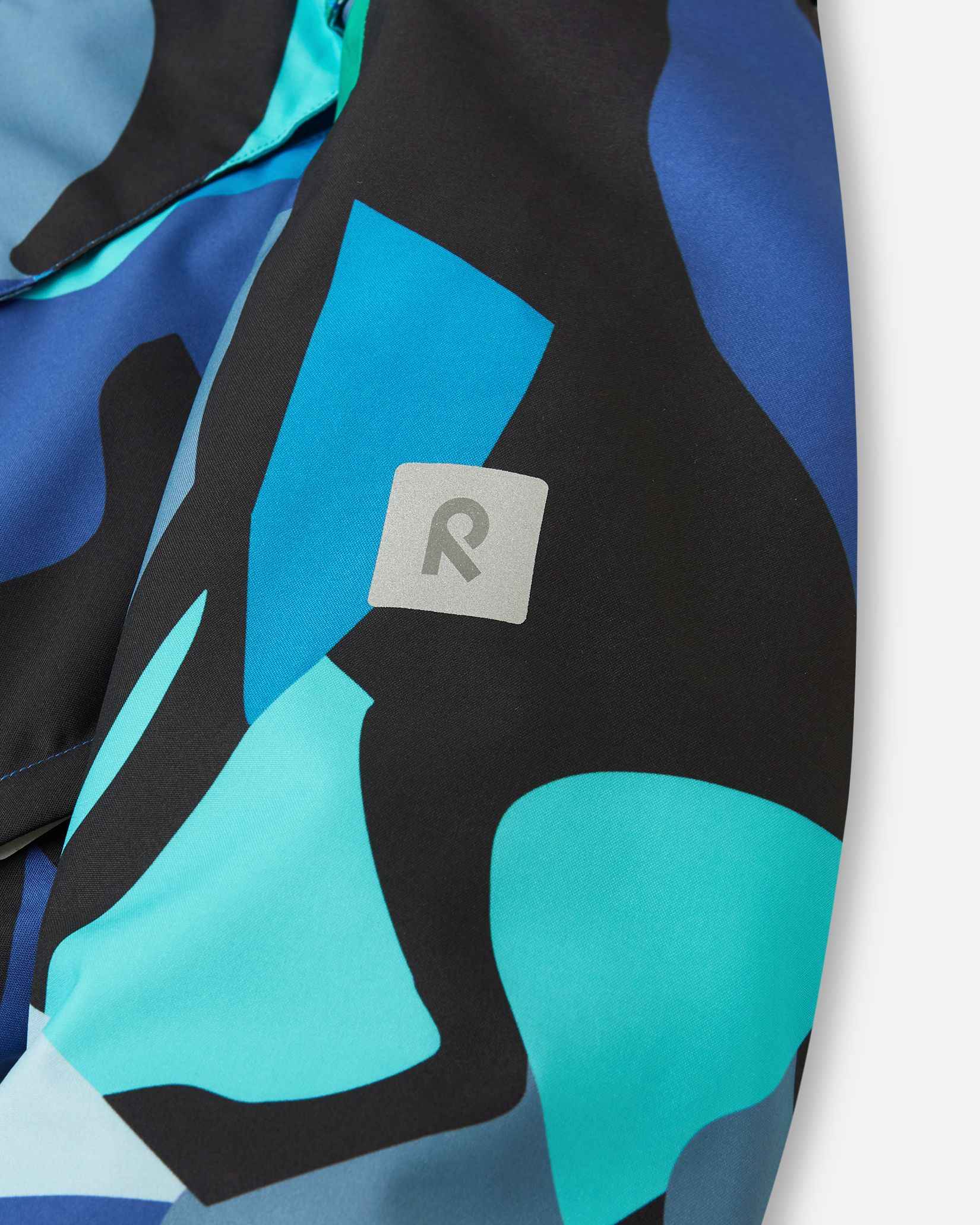 The reflective Reima R logo sits on the sleeve of the blue abstract camo coat.