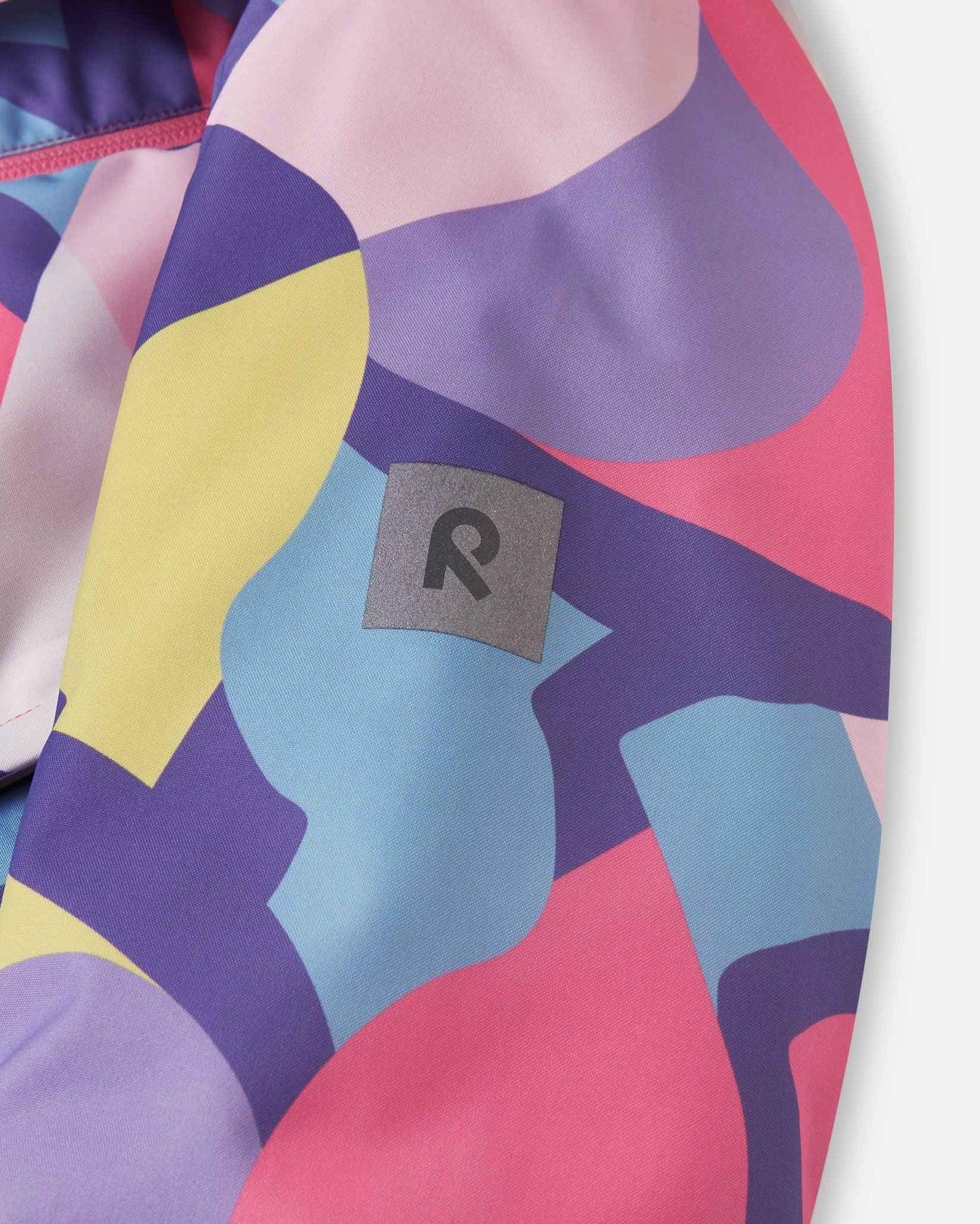 A silver Reima patch rests against the purple and yellow geometric pattern of the ski sleeve.