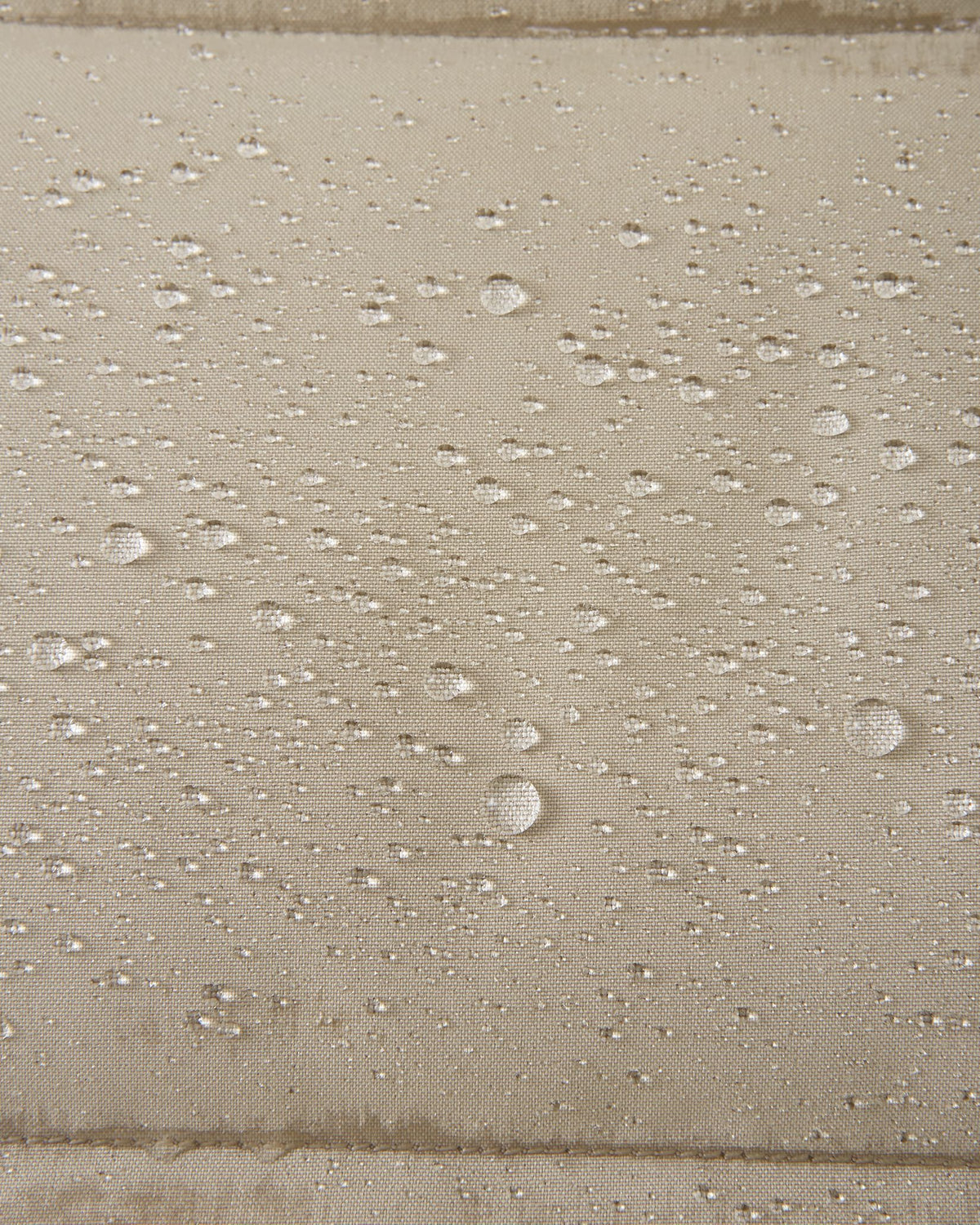 A extreme macro detail image showing multiple water droplets beading and repelling from the surface of the Reima Parkkala girls' long down winter coat in Earthy Beige, demonstrating its advanced water-repellent finish (BIONIC-FINISH® ECO technology).