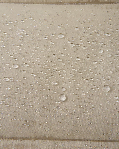 A extreme macro detail image showing multiple water droplets beading and repelling from the surface of the Reima Parkkala girls' long down winter coat in Earthy Beige, demonstrating its advanced water-repellent finish (BIONIC-FINISH® ECO technology).