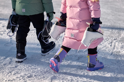 Outdoor lifestyle image of a child carrying white figure skates while wearing the warm grey pink Reima Parkkala kids' long puffer coat, showcasing its comfortable, protective knee-length fit for active winter activities on the ice.