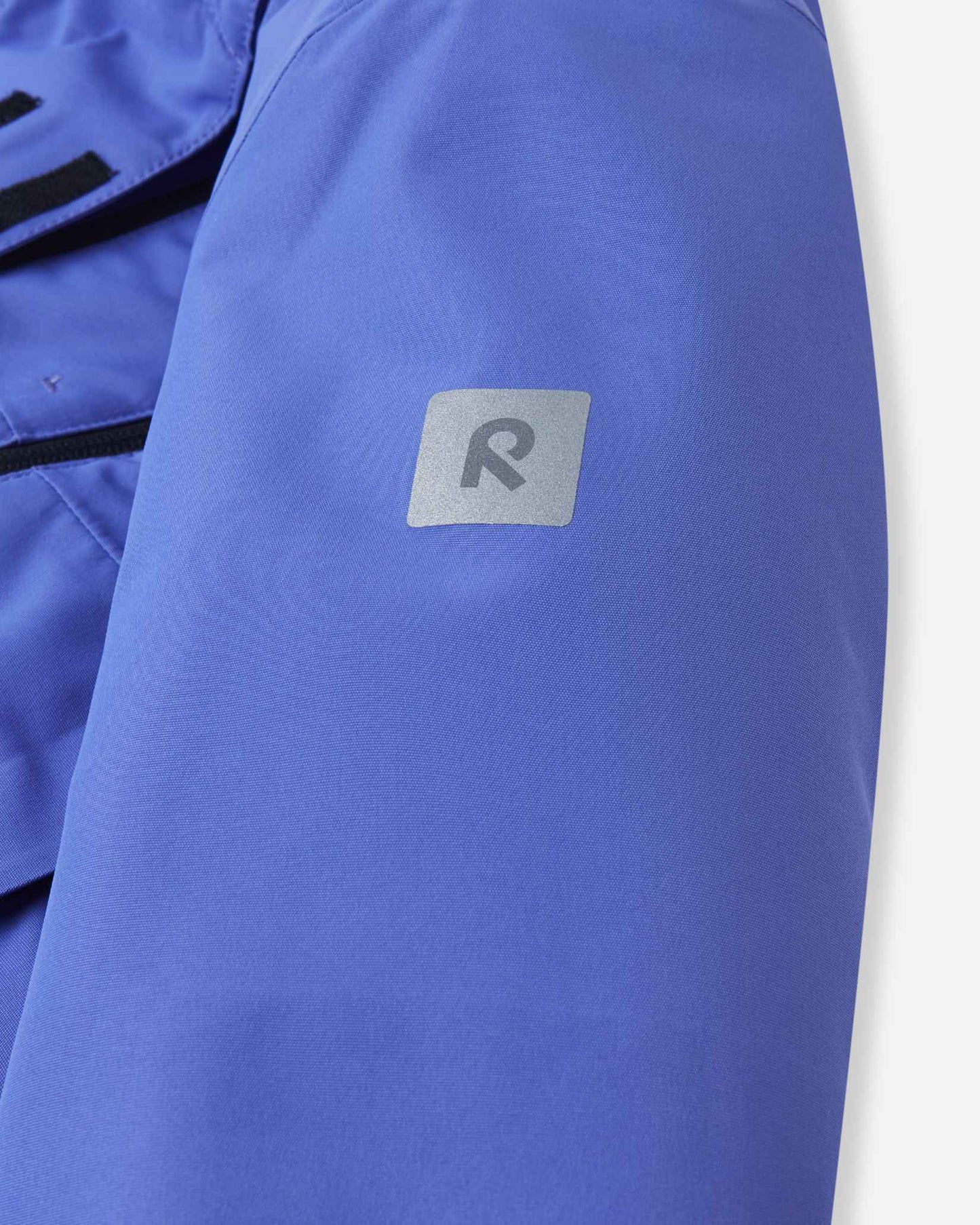 Close-up of the upper sleeve on the breezy violet Reima Perille girls' winter jacket, highlighting the square reflective Reima 'R' logo patch designed to increase child visibility and safety during dark winter days.