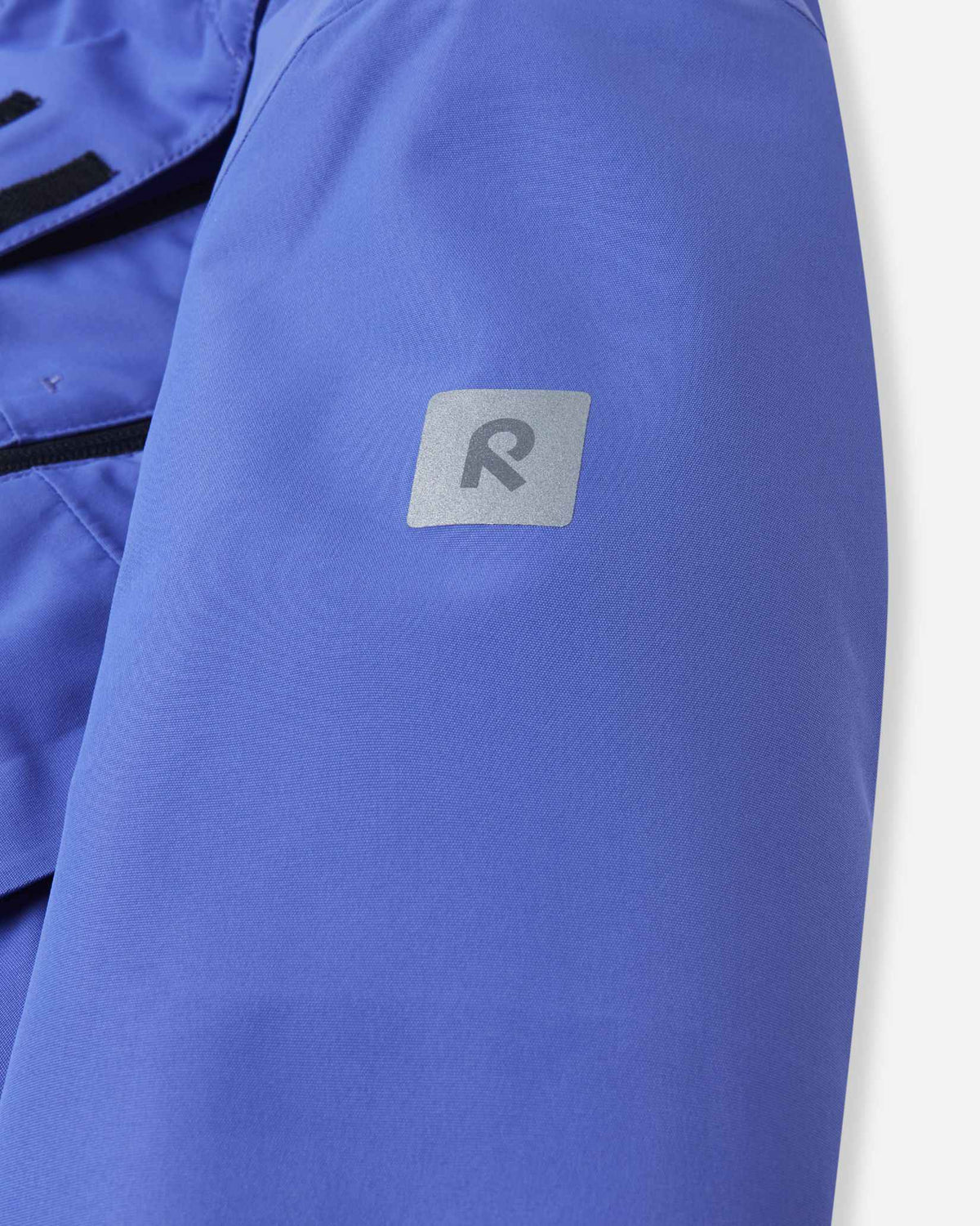 Close-up of the upper sleeve on the breezy violet Reima Perille girls' winter jacket, highlighting the square reflective Reima 'R' logo patch designed to increase child visibility and safety during dark winter days.