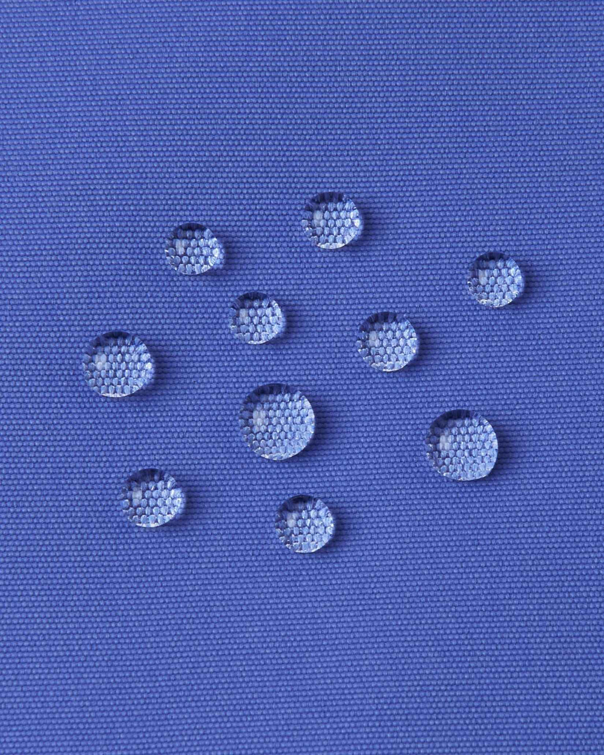 Macro photography of water droplets beading off the breezy violet outer shell of the Reima Perille ski jacket, demonstrating the high-performance BIONIC-FINISH ECO water and dirt repellent technology.