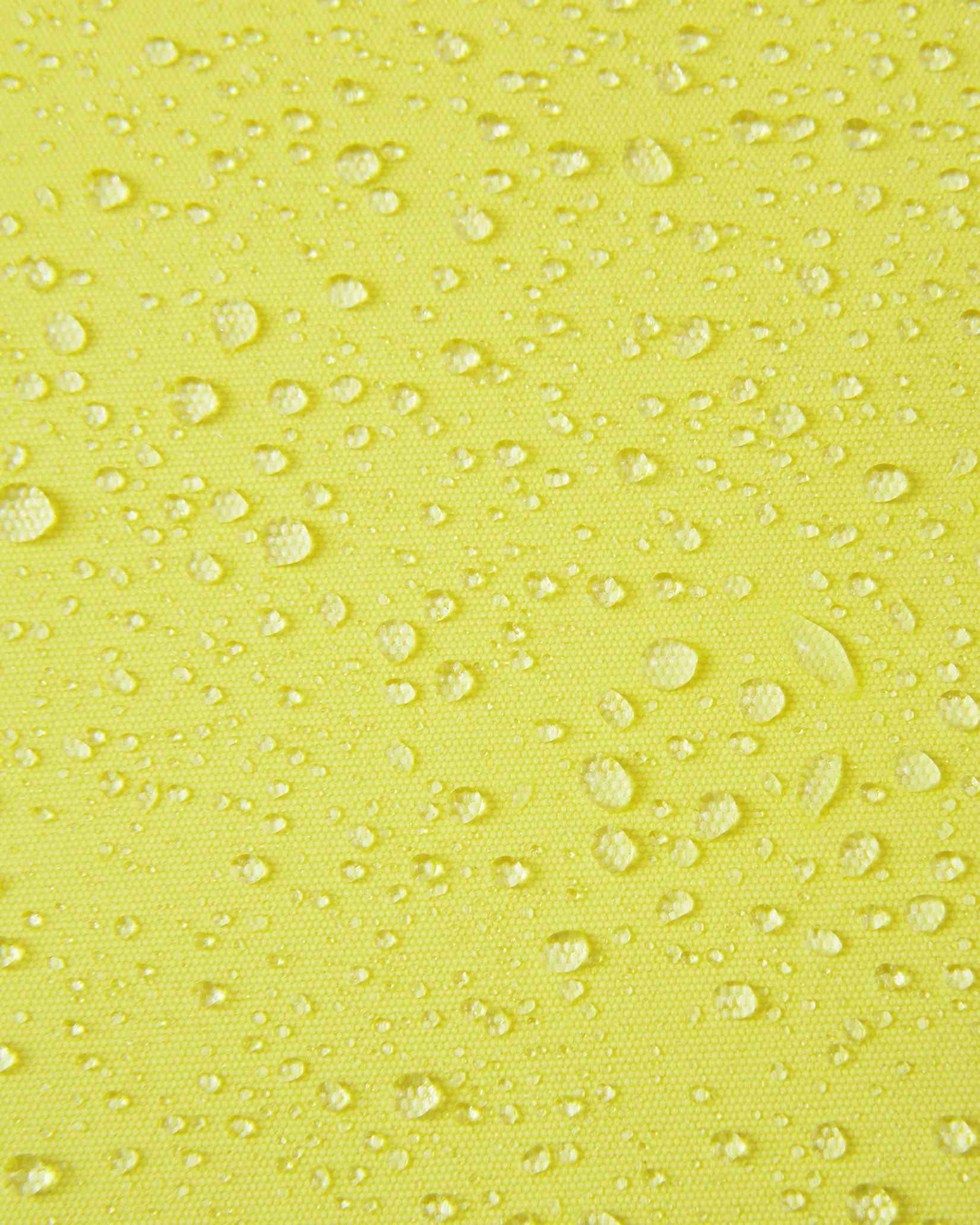Macro close-up of water droplets beading and rolling off the bright yellow outer fabric of the Reima Perille ski jacket, illustrating the high-performance breathable, windproof, and waterproof Reimatec coating.