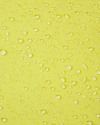 Macro close-up of water droplets beading and rolling off the bright yellow outer fabric of the Reima Perille ski jacket, illustrating the high-performance breathable, windproof, and waterproof Reimatec coating.