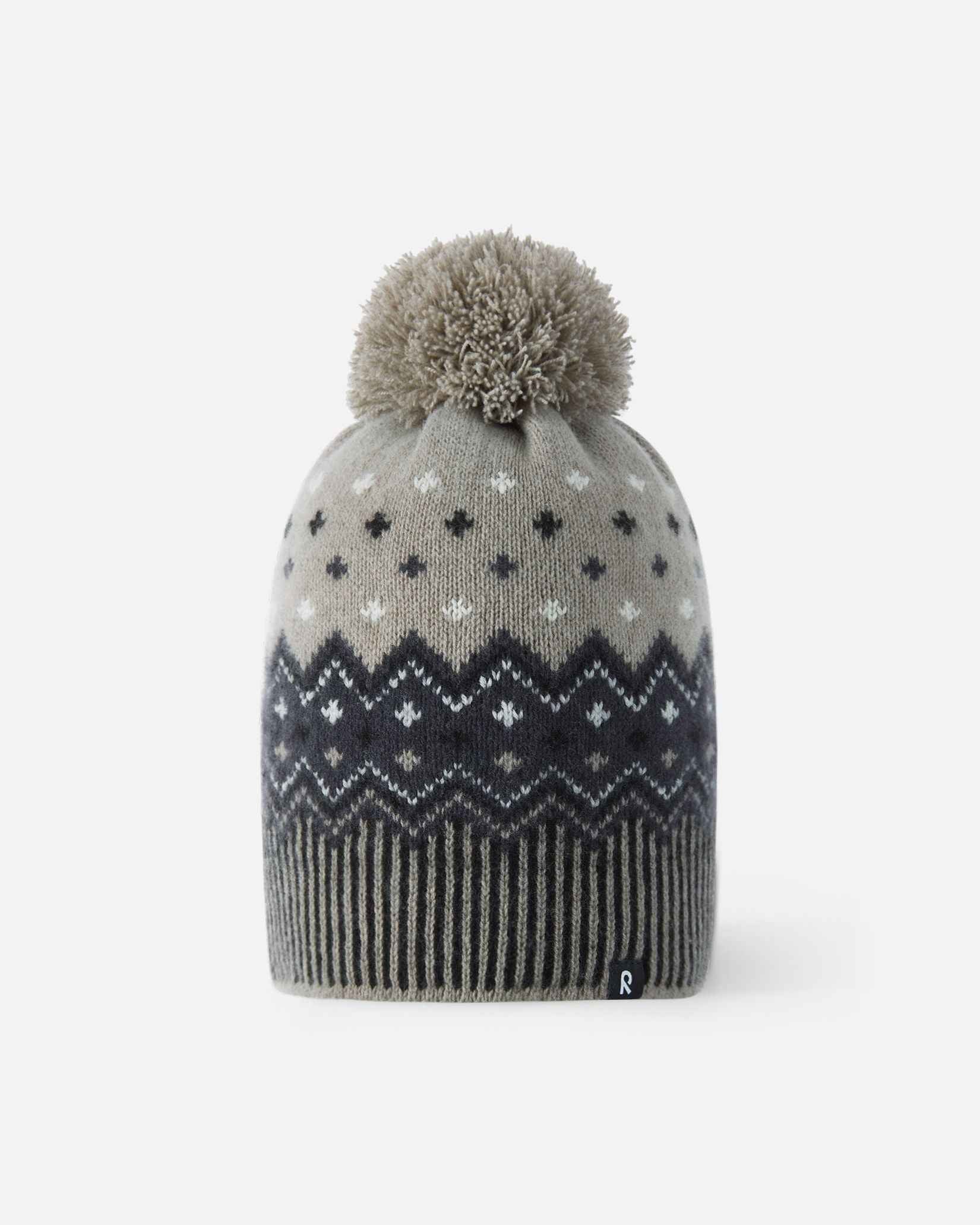 Front flat lay view of the black and charcoal Reima Pohjoinen kids' merino wool winter beanie, featuring a traditional Nordic jacquard snowflake pattern, a ribbed hem, a fluffy yarn pom-pom, and a subtle reflective logo tag.