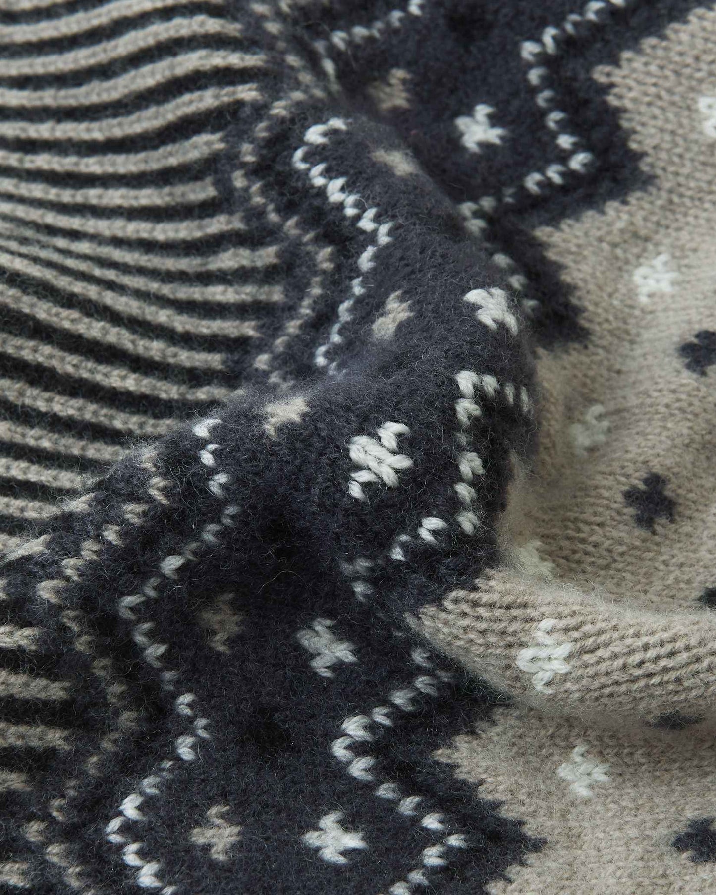 Macro close-up of the intricate jacquard knit texture on the black and charcoal Reima Pohjoinen kids' winter beanie, highlighting the soft, insulating merino wool yarn structure.