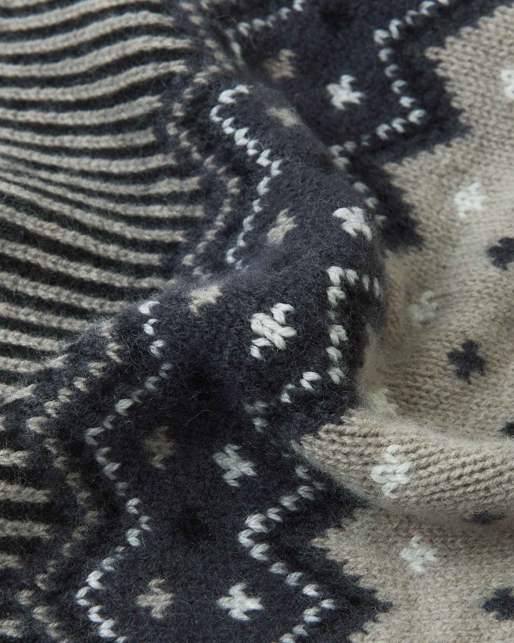 Macro close-up of the intricate jacquard knit texture on the black and charcoal Reima Pohjoinen kids' winter beanie, highlighting the soft, insulating merino wool yarn structure.