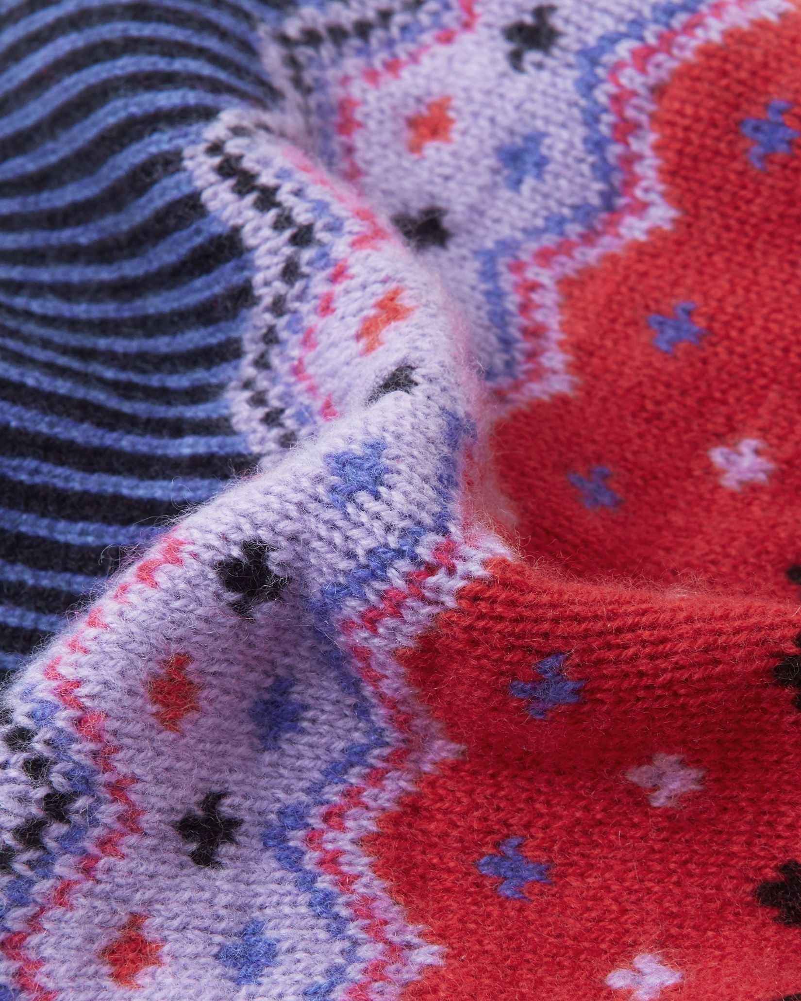 Macro close-up of the premium red, purple, and navy merino wool knit on the Reima Pohjoinen kids' beanie, demonstrating the soft yarn density and rich colorful pattern.