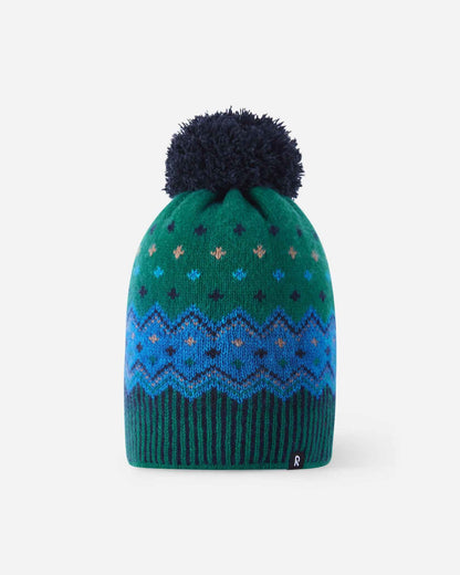 Front flat lay view of the navy and pine green Reima Pohjoinen kids' merino wool beanie, displaying a vibrant blue and green Nordic geometric pattern, ribbed hem, navy pom-pom, and reflective logo badge.