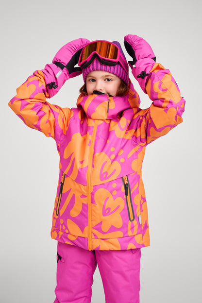A young girl modeling the Reima Posio waterproof ski jacket in fuchsia and orange floral print, fully geared for winter sports with matching fuchsia snow pants, ski goggles, a knit beanie, and winter gloves.