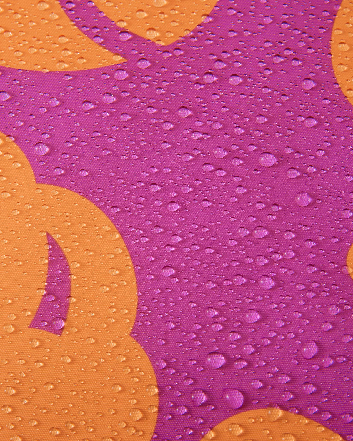 Macro detail of the fuchsia and orange floral patterned Reimatec fabric on the Reima Posio girls' ski jacket, showing dense water droplets beading on the surface to demonstrate its waterproof capabilities.