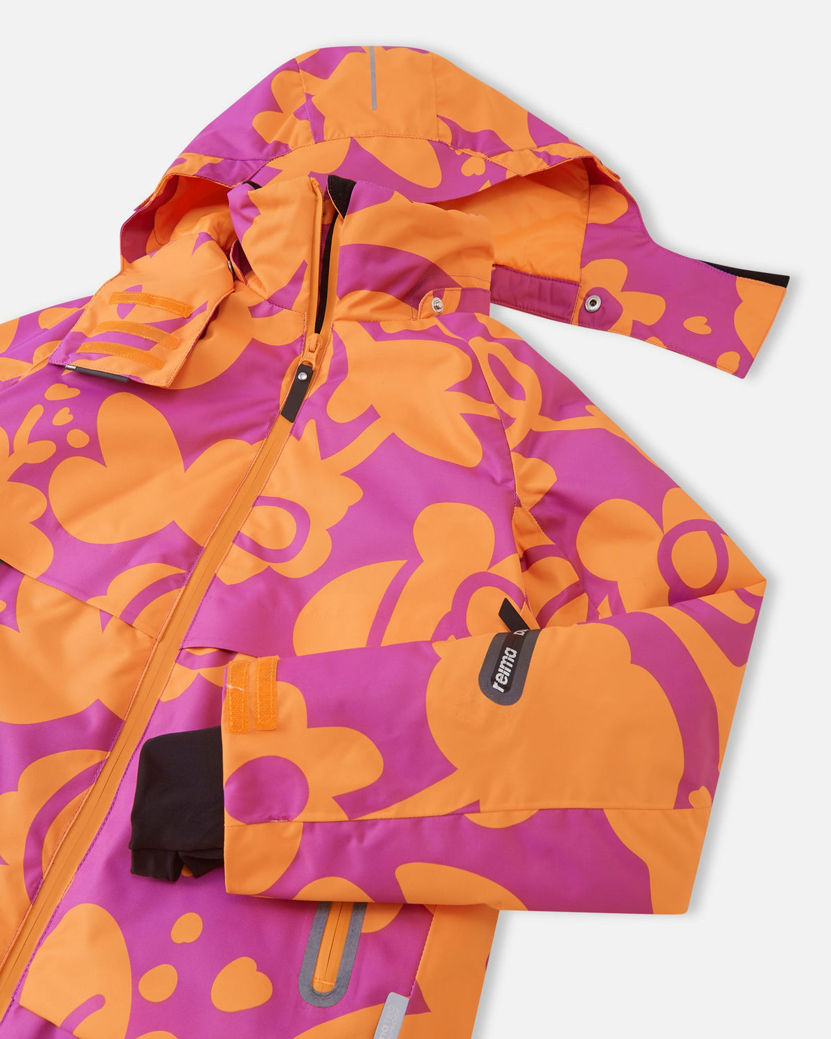 Close-up of the upper chest on the Reima Posio girls' ski jacket, detailing the snap buttons for the detachable hood, the protective front zipper wind flap, and the left sleeve ski pass pocket.