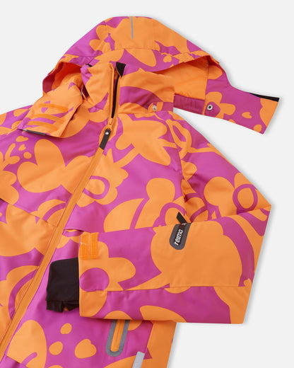 Close-up of the upper chest on the Reima Posio girls' ski jacket, detailing the snap buttons for the detachable hood, the protective front zipper wind flap, and the left sleeve ski pass pocket.