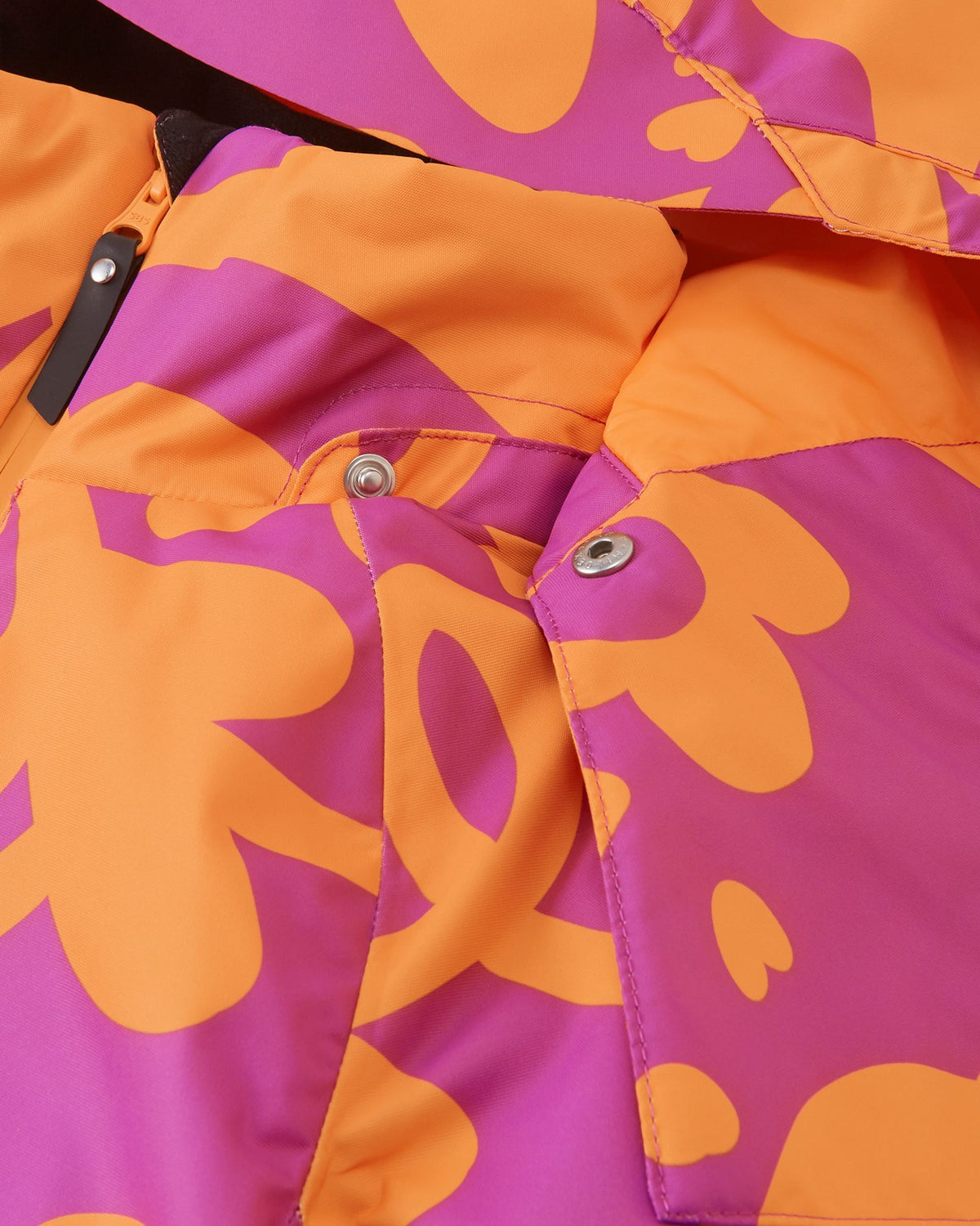 Macro detail shot of the collar on the Reima Posio girls' ski jacket, highlighting the secure metallic snap buttons used to attach the removable hood to the fuchsia floral fabric.