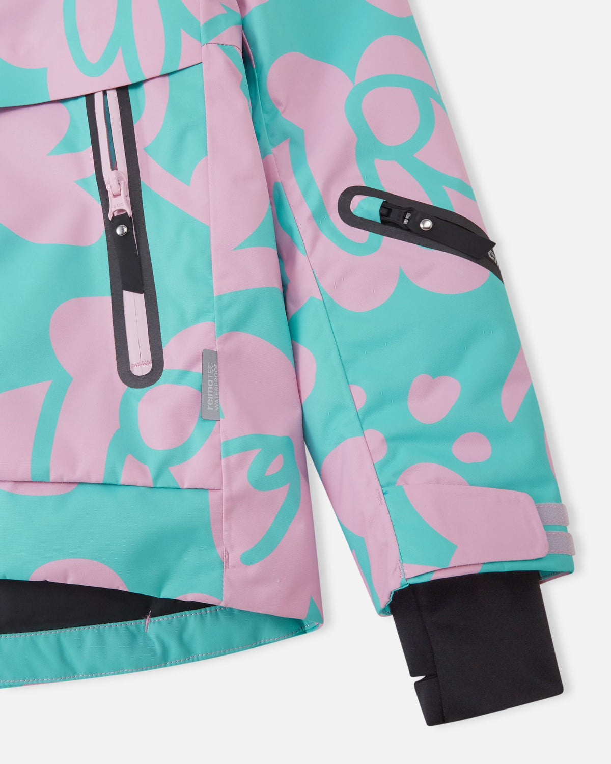 Close-up of the sleeve on the Reima Posio girls' ski jacket, showing the adjustable Velcro outer cuff, black Lycra inner cuff with thumbhole, front zippered pocket, and the Reimatec waterproof authenticity tag.