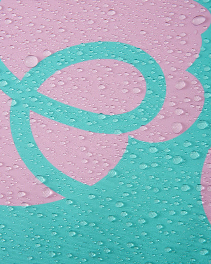 Macro detail of the light heather pink and teal floral Reimatec fabric used on the Reima Posio girls' ski jacket, demonstrating its waterproof technology with dense water droplets beading and resting on the surface.