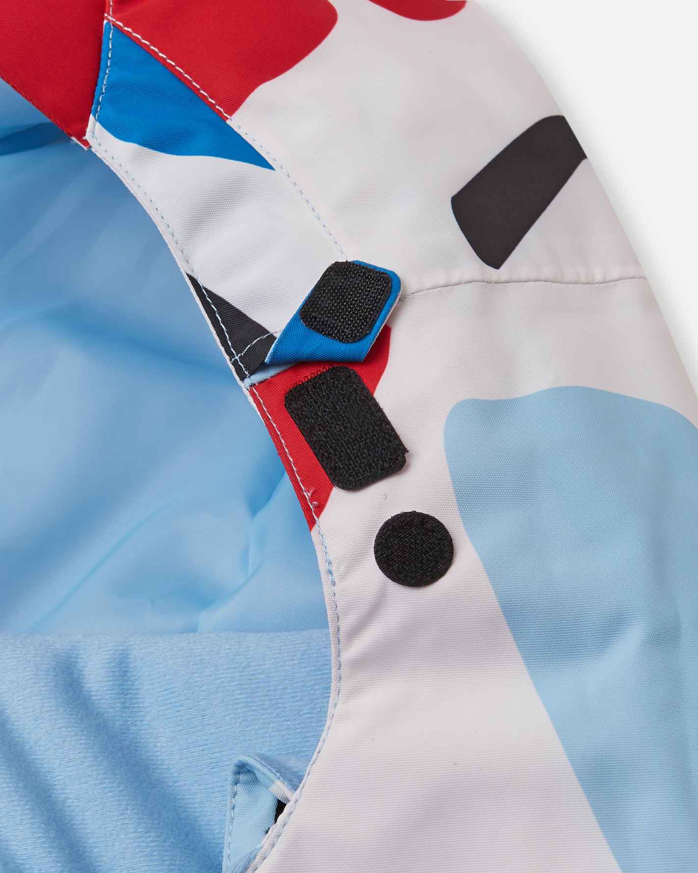 Detailed look at the secure velcro hood fasteners and protective neck baffle on the white floral Reima Posio kids' breathable ski jacket, ensuring a completely draft-free fit around the face.