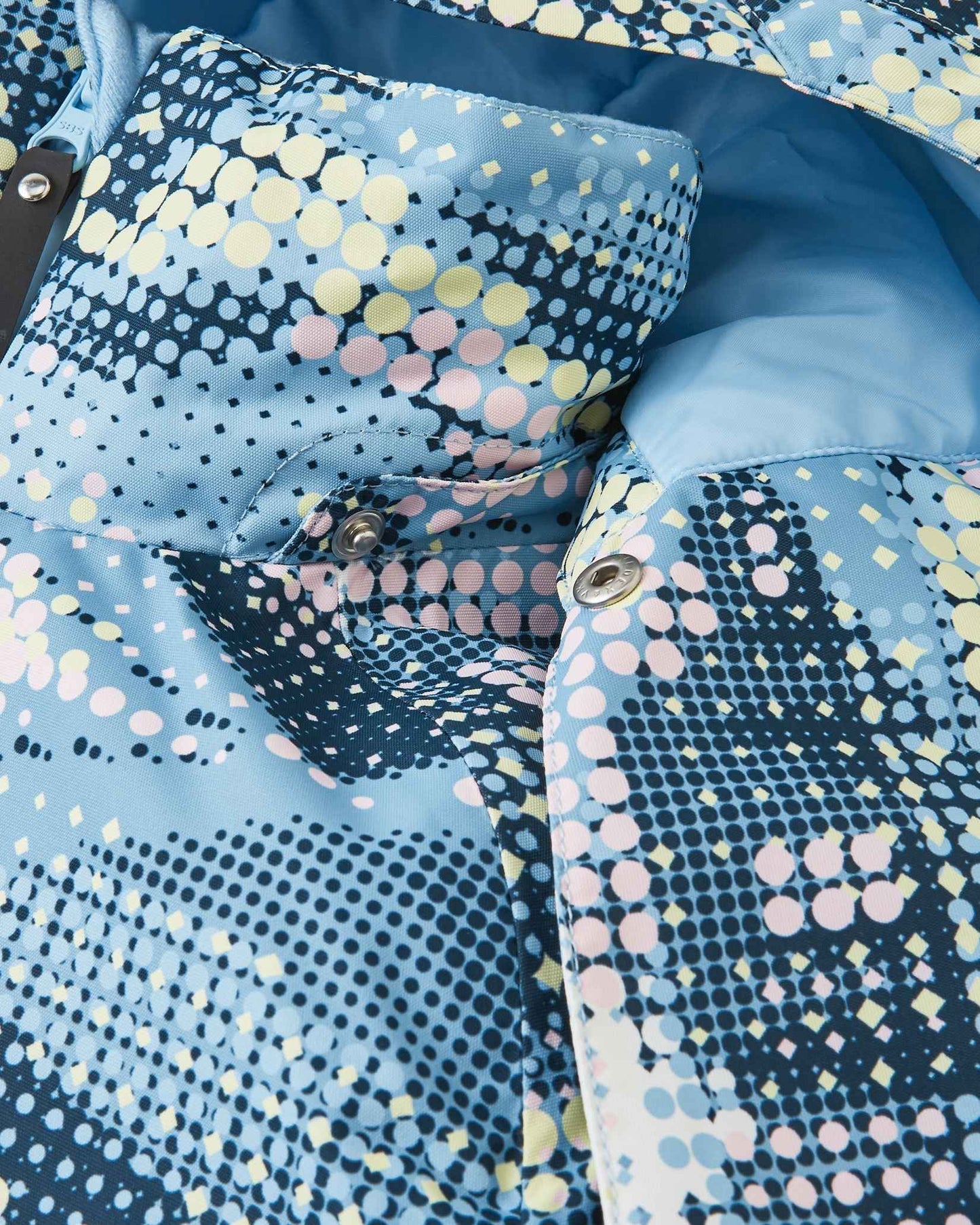 Close-up detail of the protective chin guard and secure collar snap buttons on the frozen blue Reima Posio kids' waterproof ski jacket, highlighting the durable hardware and intricate digital pattern.