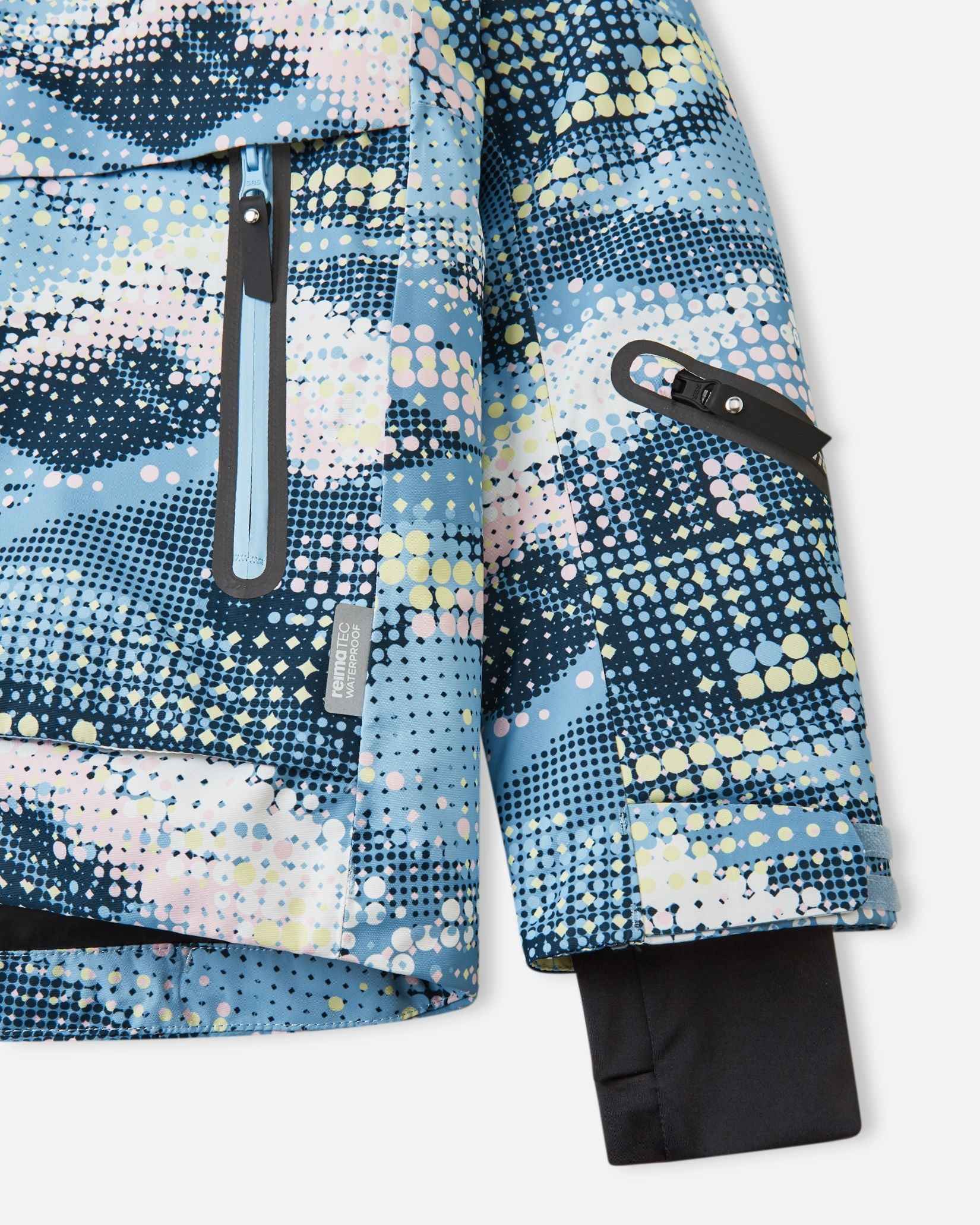 Detail view of the waterproof zippered sleeve ski pass pocket, velcro cuff adjuster, and inner lycra cuff with thumbhole on the frozen blue Reima Posio kids' ski jacket.