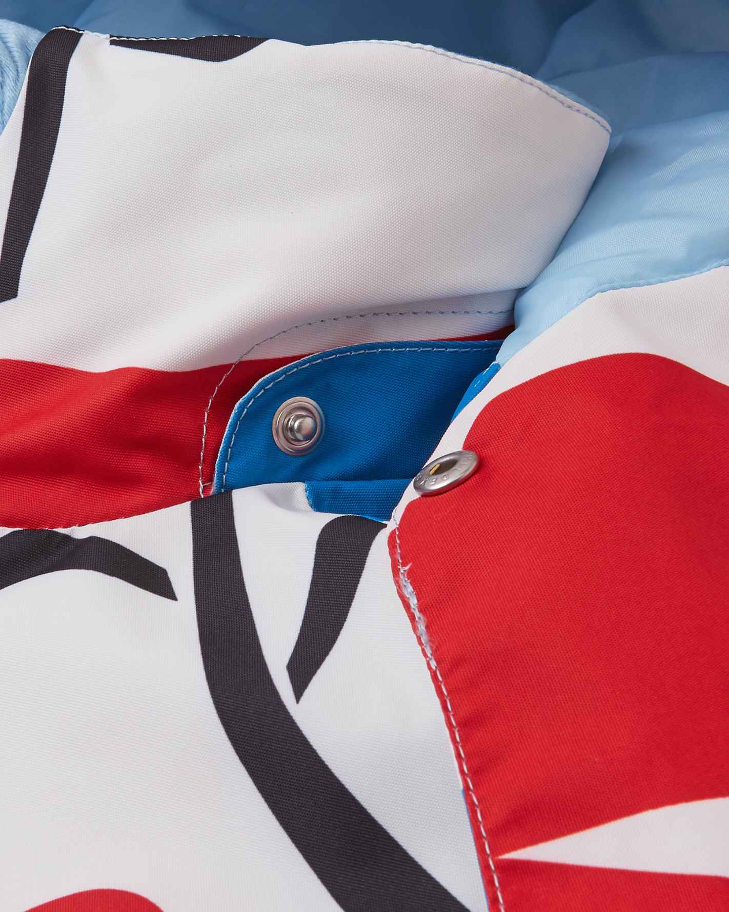 Close-up detail of the protective chin guard and secure collar snap buttons on the white Reima Posio kids' waterproof ski jacket, highlighting the durable hardware and bright floral print.
