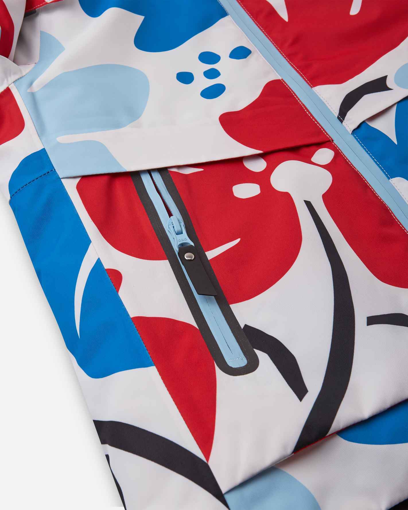 Close-up of the sealed, water-resistant zipper pocket on the front panel of the white Reima Posio kids' winter ski jacket, showcasing the durable construction and bright floral design.