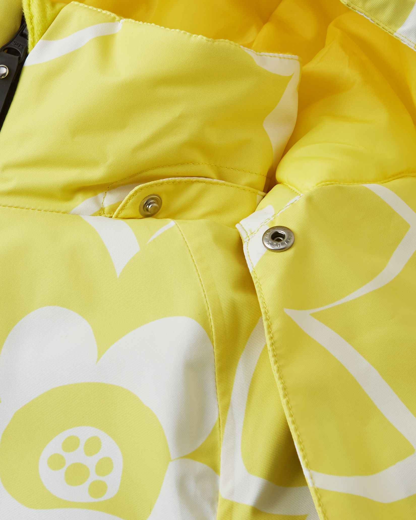 Close-up detail of the protective chin guard and secure collar snap buttons on the yellow Reima Posio kids' waterproof ski jacket, highlighting the durable hardware and bright white floral print.