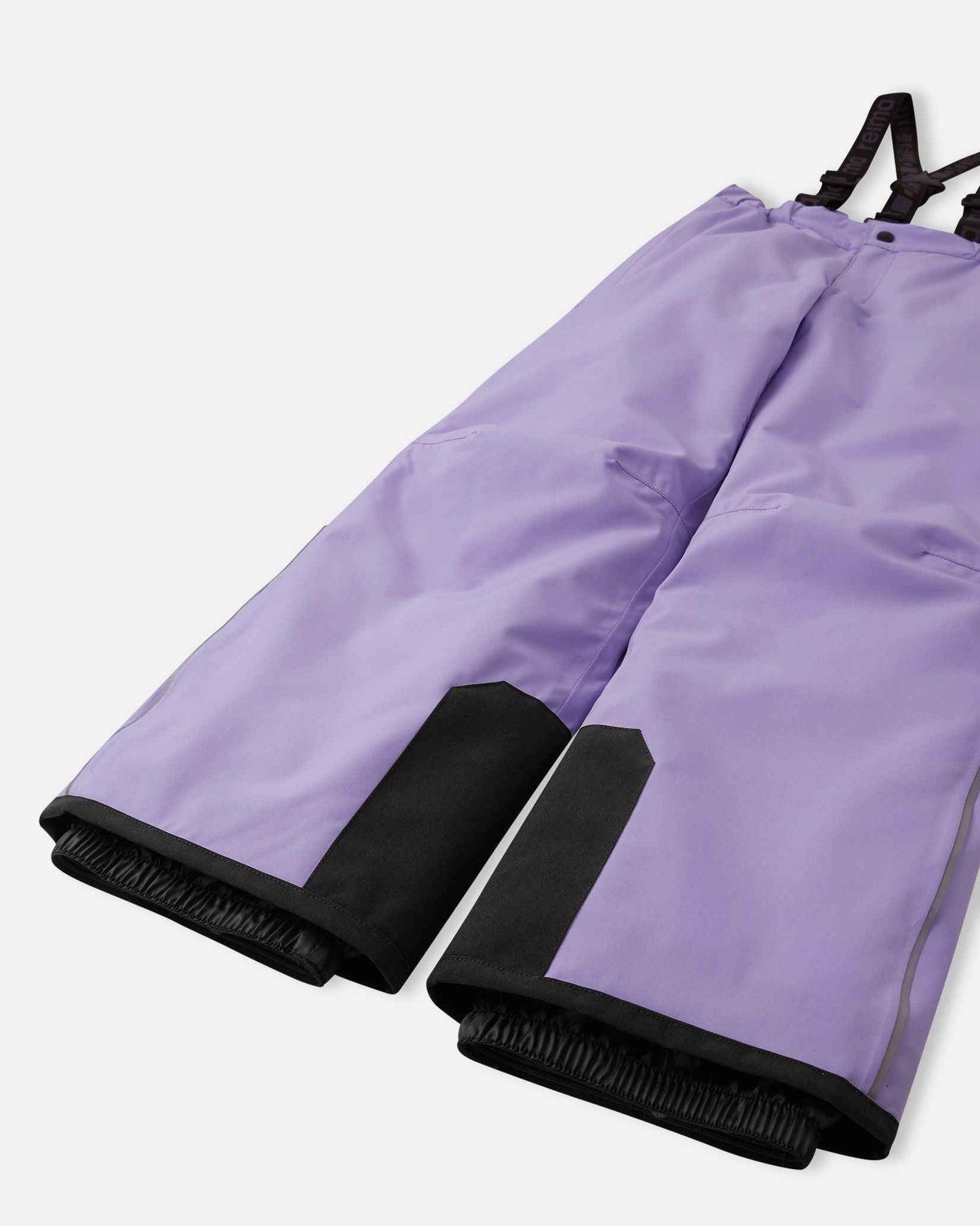 Detail view of the lower legs on the blooming lilac Reima Proxima kids' ski pants, emphasizing the rugged black reinforced hems to protect against ski edges and the inner elastic snow locks designed to securely grip boots and keep powder out.