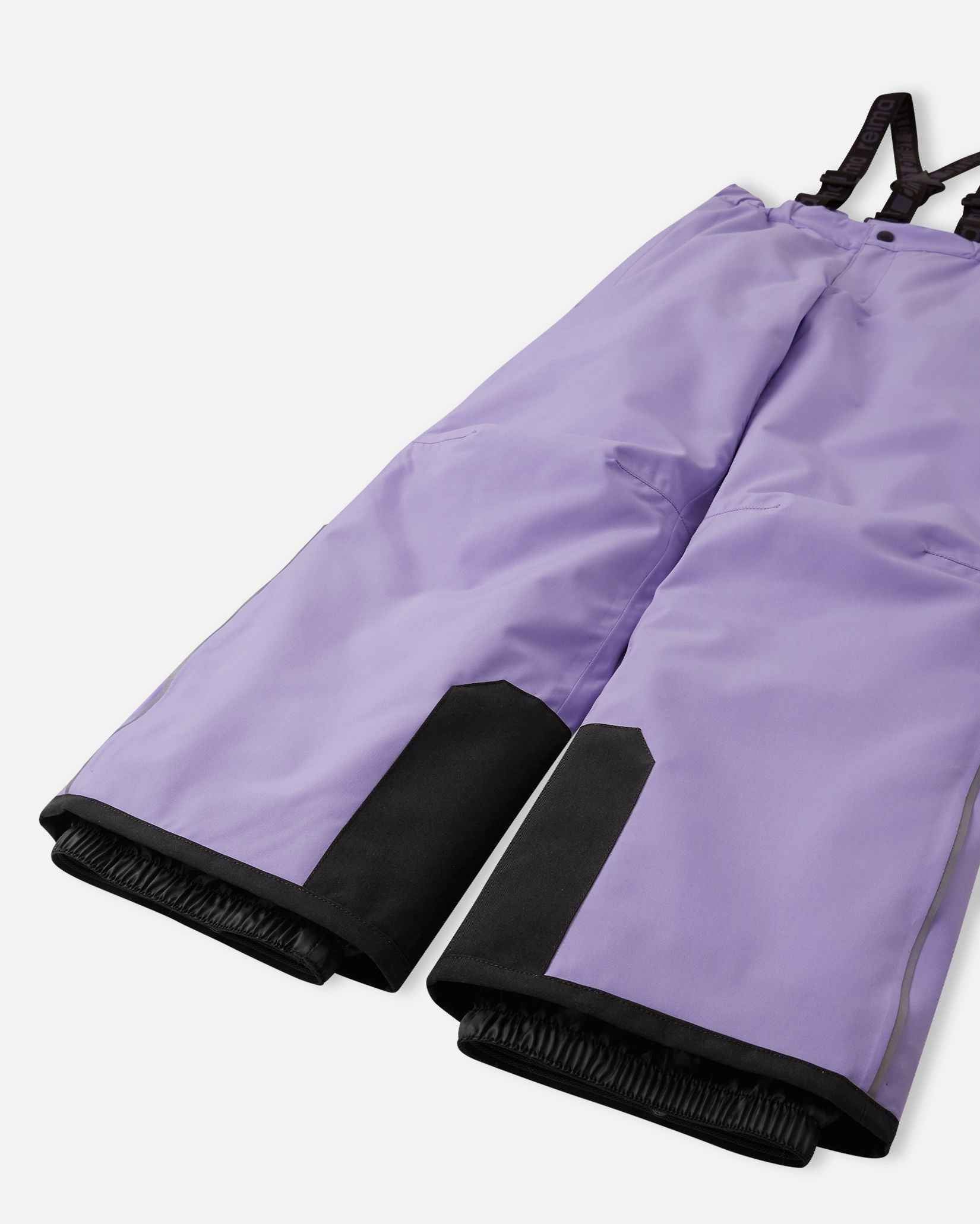 Detail view of the lower legs on the blooming lilac Reima Proxima kids' ski pants, emphasizing the rugged black reinforced hems to protect against ski edges and the inner elastic snow locks designed to securely grip boots and keep powder out.