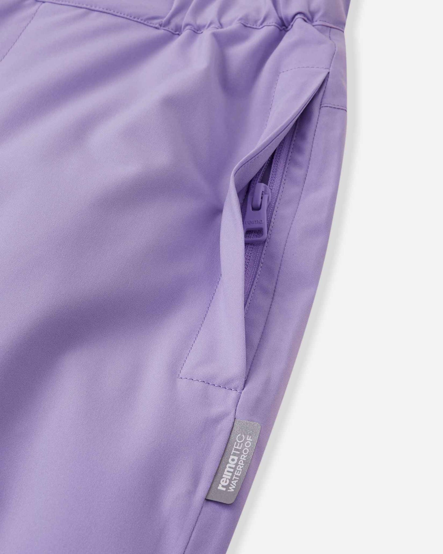 Close-up detail of the hip on the blooming lilac Reima Proxima kids' ski pants, highlighting a secure, low-profile zippered pocket and a Reimatec waterproof quality tag.