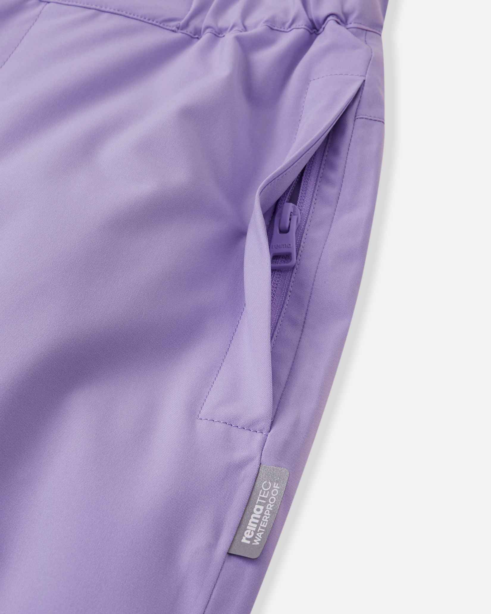 Close-up detail of the hip on the blooming lilac Reima Proxima kids' ski pants, highlighting a secure, low-profile zippered pocket and a Reimatec waterproof quality tag.