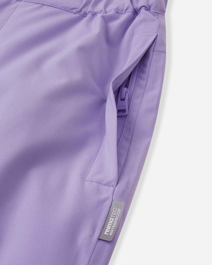 Close-up detail of the hip on the blooming lilac Reima Proxima kids' ski pants, highlighting a secure, low-profile zippered pocket and a Reimatec waterproof quality tag.