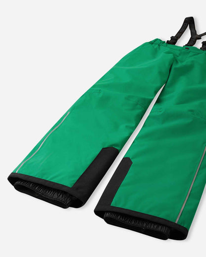 Detail view of the lower legs on the bright green Reima Proxima kids' ski pants, emphasizing the rugged black reinforced hems to protect against ski edges and the inner elastic snow locks designed to securely grip boots and keep powder out.