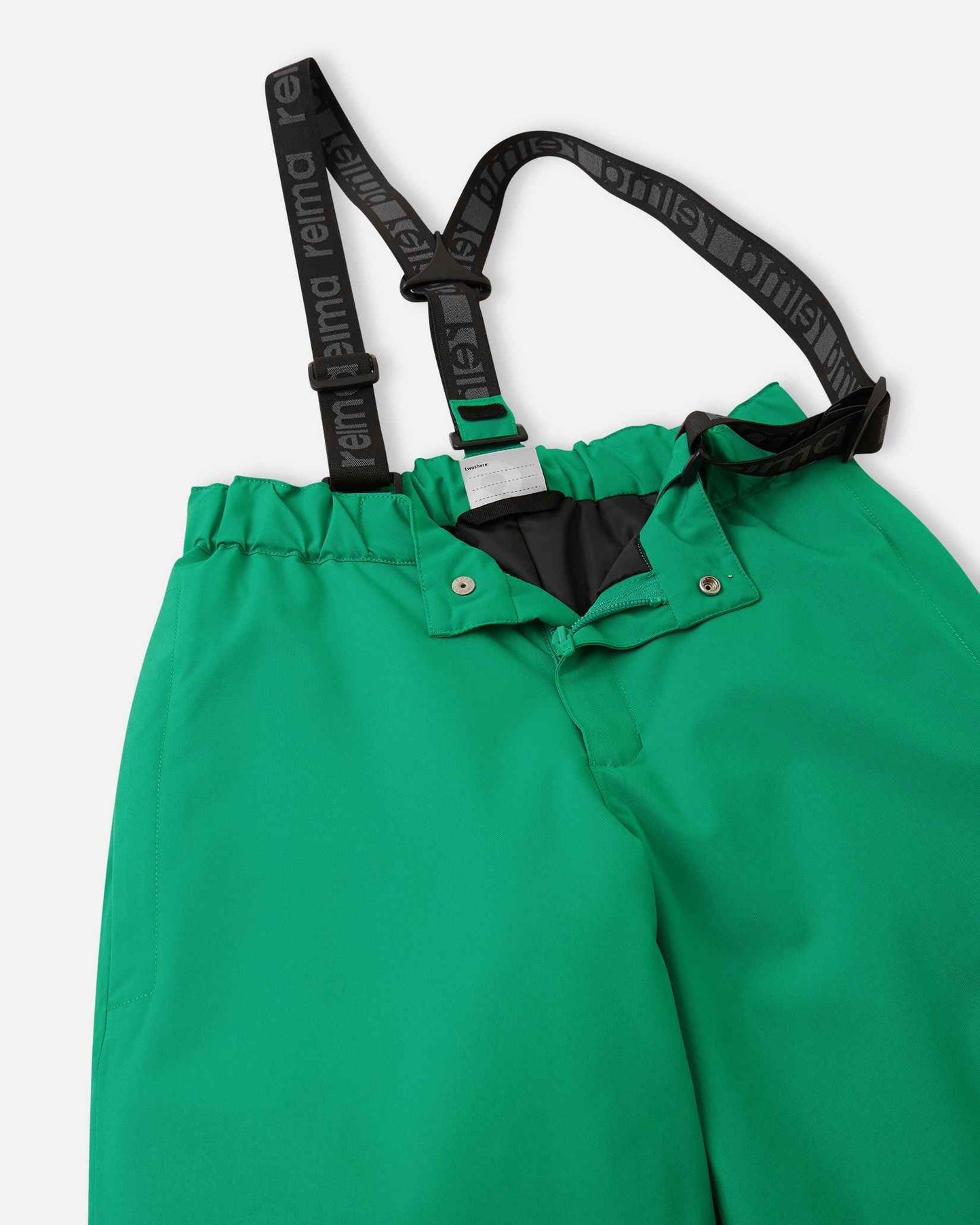 Close-up detail of the front waist on the bright green Reima Proxima kids' ski pants, showing the secure snap buttons, smooth zipper fly, elastic back waistband, and adjustable branded suspenders.
