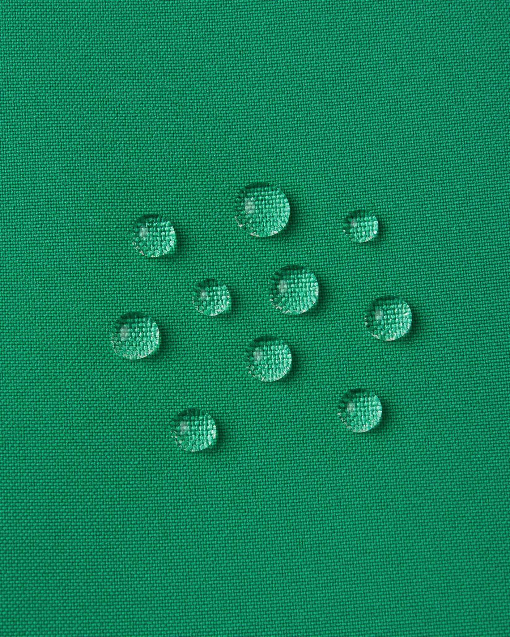 Macro close-up of water droplets actively beading and rolling off the bright green outer shell of the Reima Proxima kids' ski pants, visually highlighting the high-performance breathable and waterproof Reimatec technology.