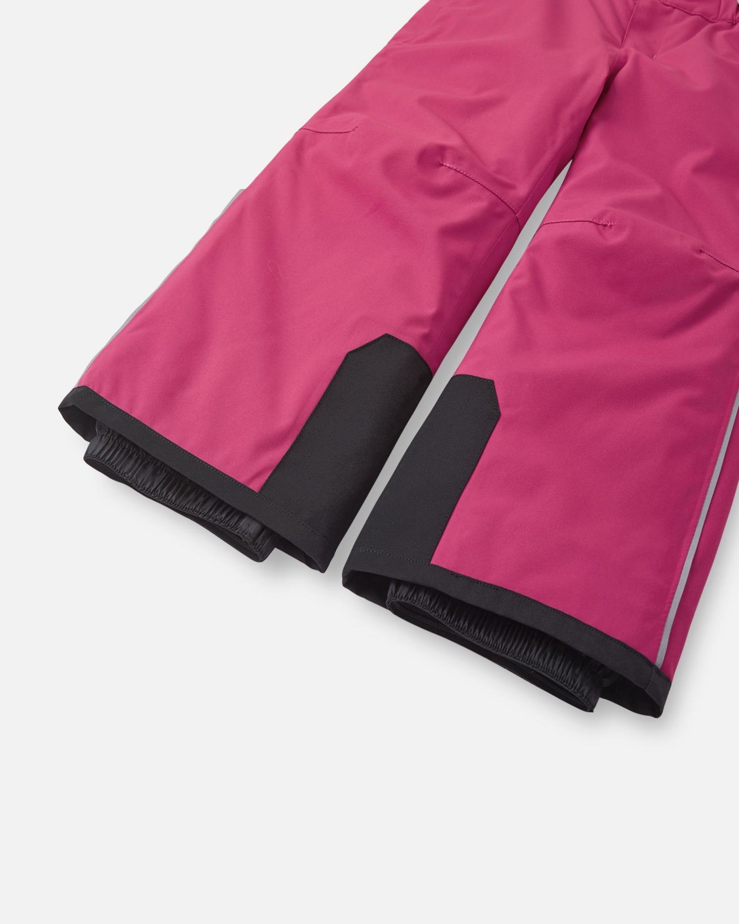 Detail view of the lower legs on the rosy berry Reima Proxima kids' ski pants, emphasizing the rugged black reinforced hems to protect against ski edges and the inner elastic snow locks designed to securely grip boots and keep powder out.