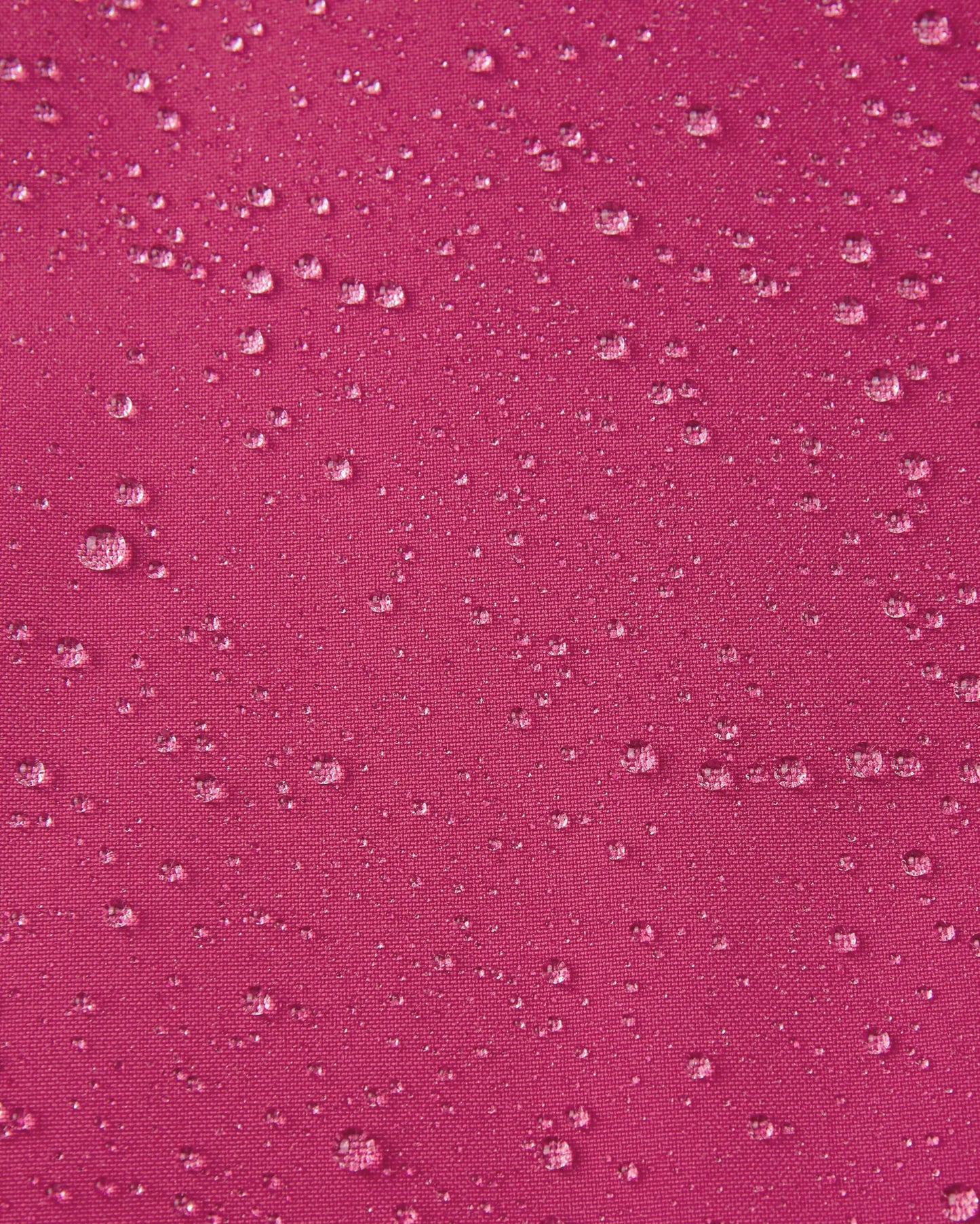 Macro close-up of water droplets actively beading and rolling off the rosy berry outer shell of the Reima Proxima kids' ski pants, visually highlighting the high-performance breathable and waterproof Reimatec technology.