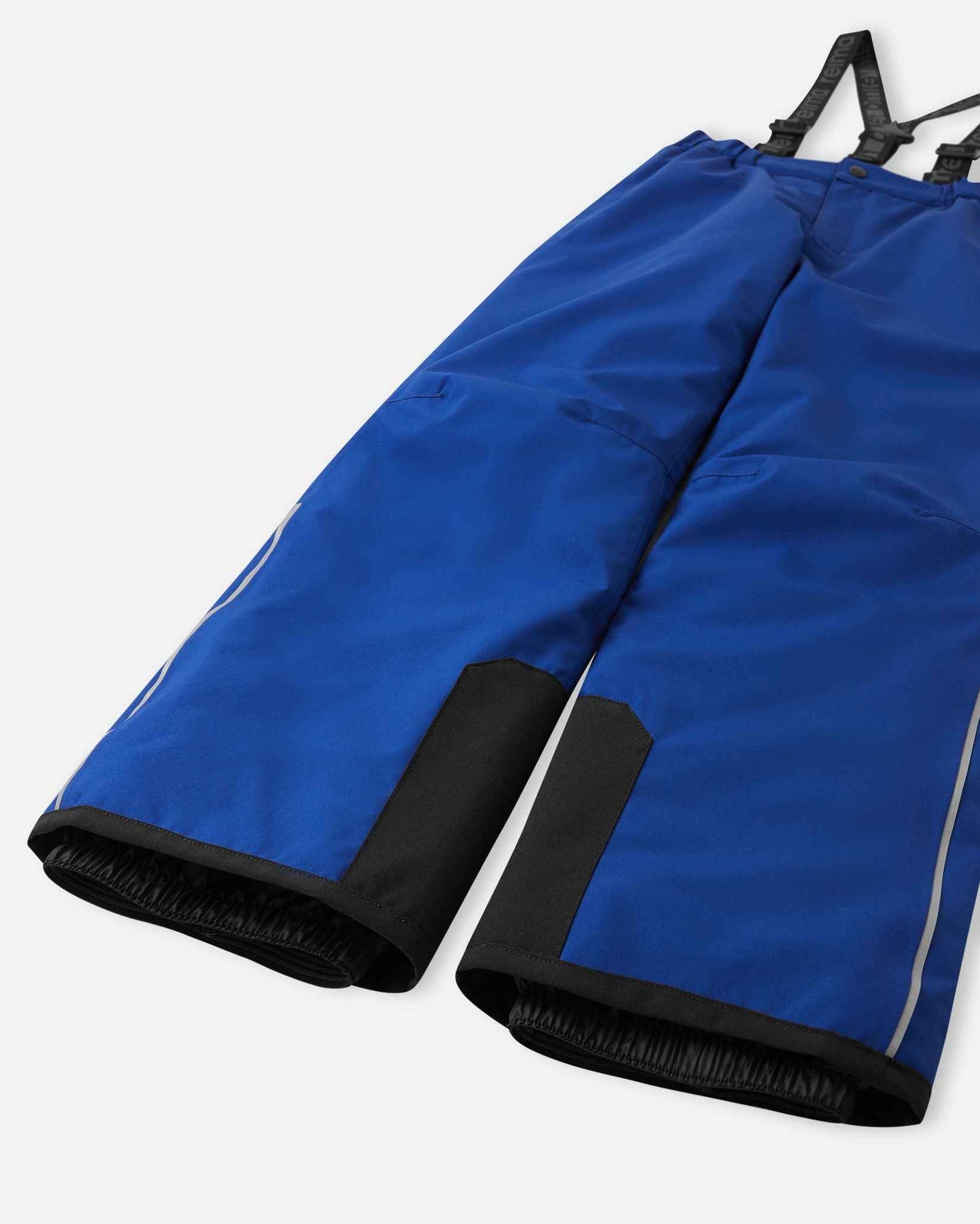 Detail view of the lower legs on the twilight blue Reima Proxima kids' ski pants, emphasizing the rugged black reinforced hems to protect against ski edges and the inner elastic snow locks designed to securely grip boots and keep powder out.