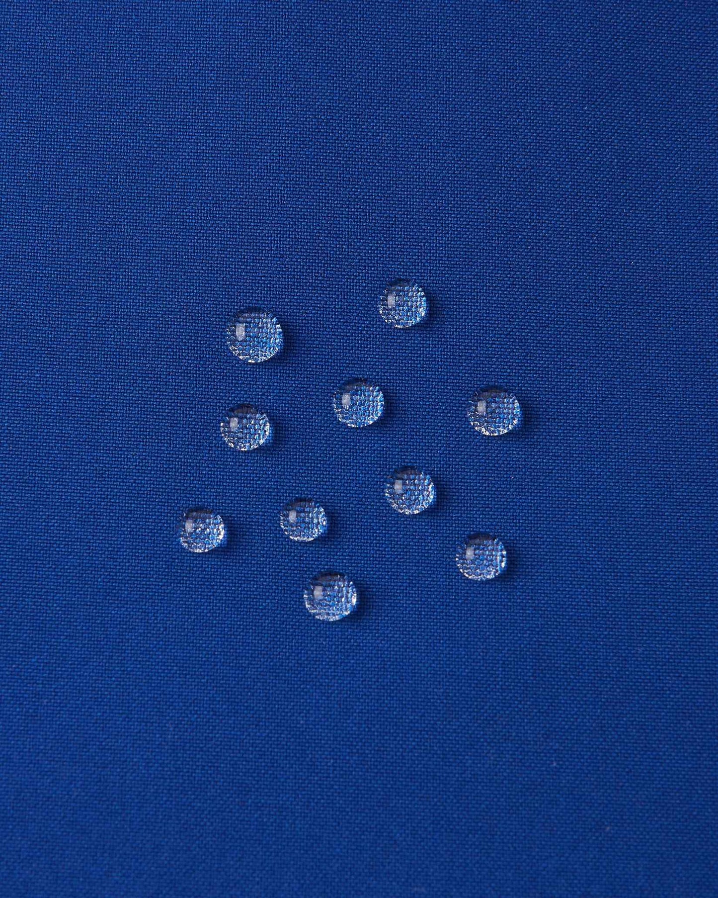 Macro close-up of water droplets actively beading and rolling off the twilight blue outer shell of the Reima Proxima kids' ski pants, visually highlighting the high-performance breathable and waterproof Reimatec technology.