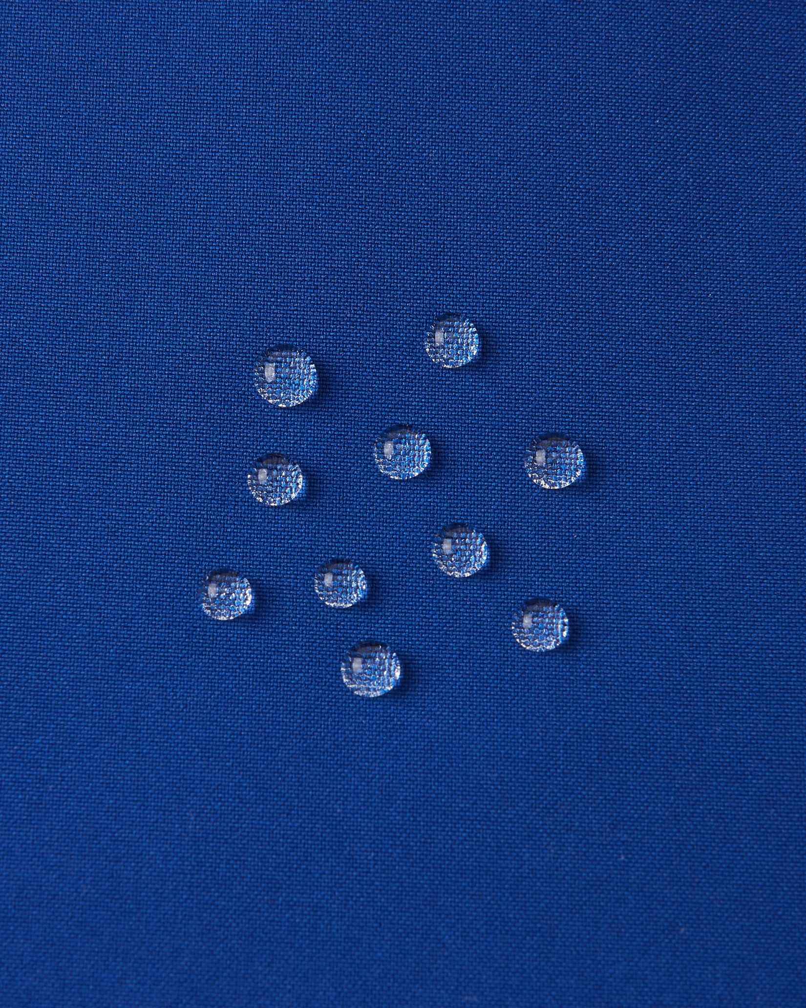 Macro close-up of water droplets actively beading and rolling off the twilight blue outer shell of the Reima Proxima kids' ski pants, visually highlighting the high-performance breathable and waterproof Reimatec technology.