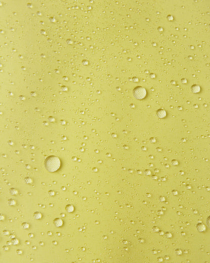 Macro close-up of water droplets actively beading and rolling off the bright yellow outer shell of the Reima Proxima kids' ski pants, visually highlighting the high-performance breathable and waterproof Reimatec technology.