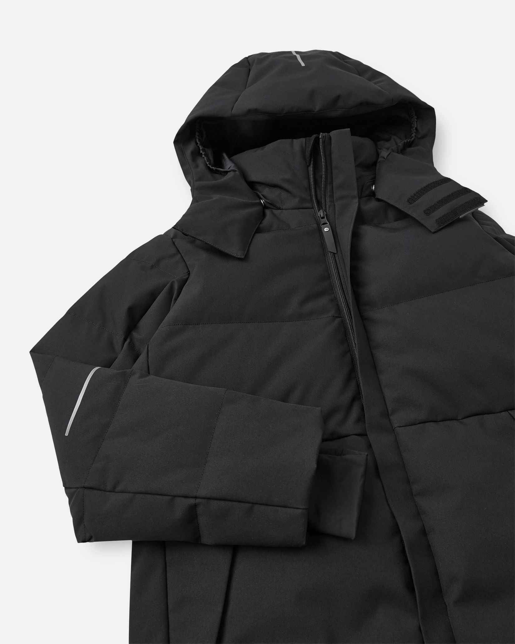 Close-up of the upper half of the Reima Ranua kids' down ski jacket in black, detailing the high protective collar, the main front zipper, and adjustable velcro tabs on the insulated hood for a secure fit.