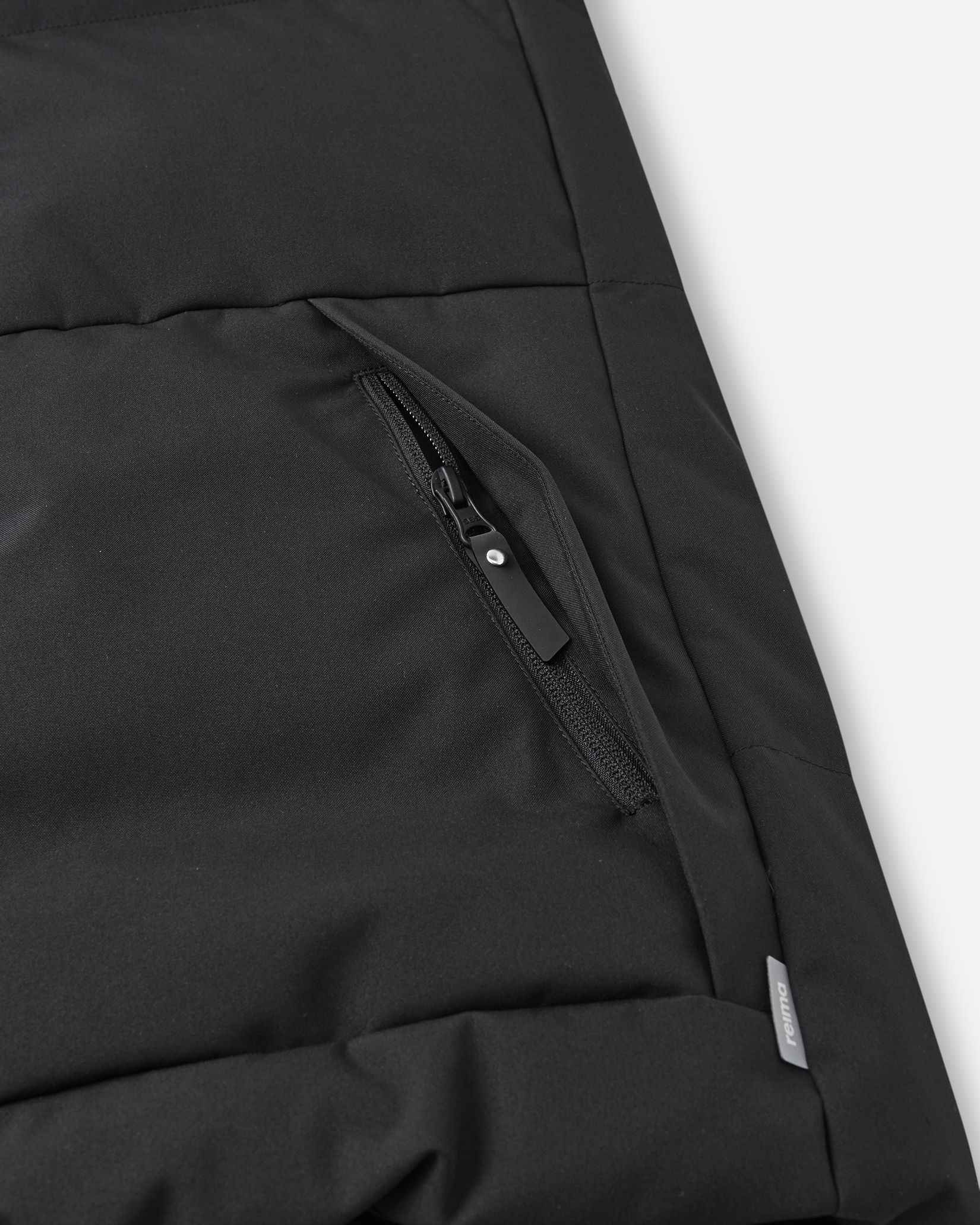 Close-up detail of the secure, hidden front zippered pocket on the quilted black body of the Reima Ranua kids' down ski jacket, perfect for safely storing small items.