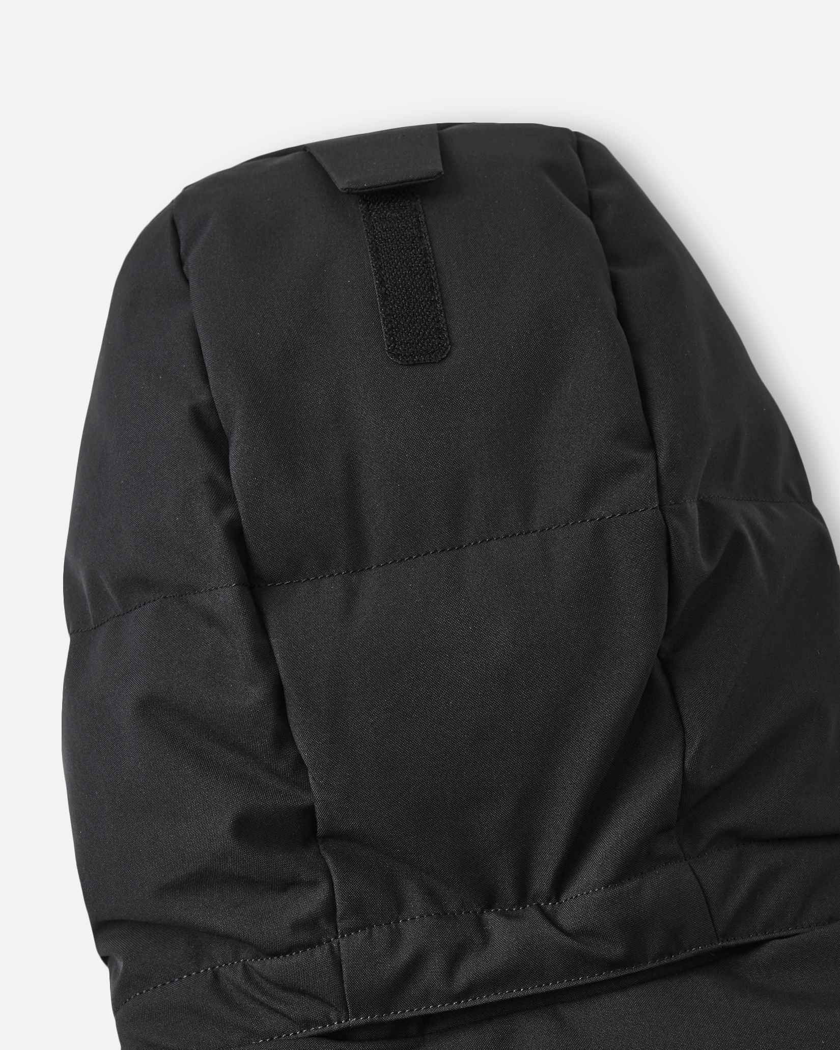 Close-up of the back of the insulated hood on the black Reima Ranua kids' down ski jacket, detailing the velcro adjustment tab used to customize the fit for maximum warmth and visibility.