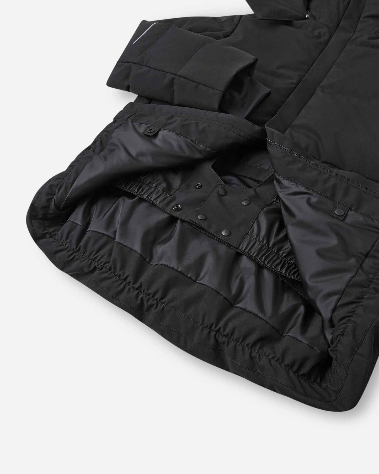 Interior view of the lower half of the black Reima Ranua kids' down ski jacket, featuring a smooth black lining, an adjustable elastic hem, and a built-in snow skirt with snap fasteners to completely block out snow and cold drafts.