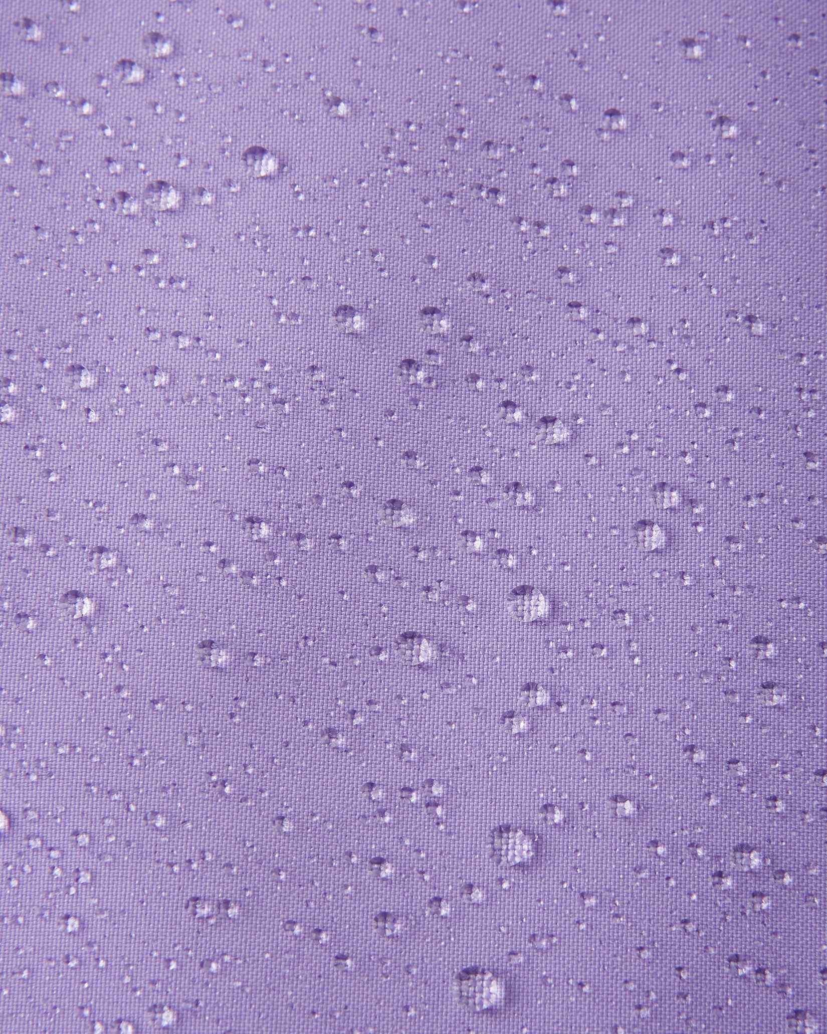 A detailed close-up texture shot of water droplets beading up cleanly on the blooming lilac water-repellent fabric of a Reima Ranua kids' down ski jacket, demonstrating its durable weather-resistant performance.