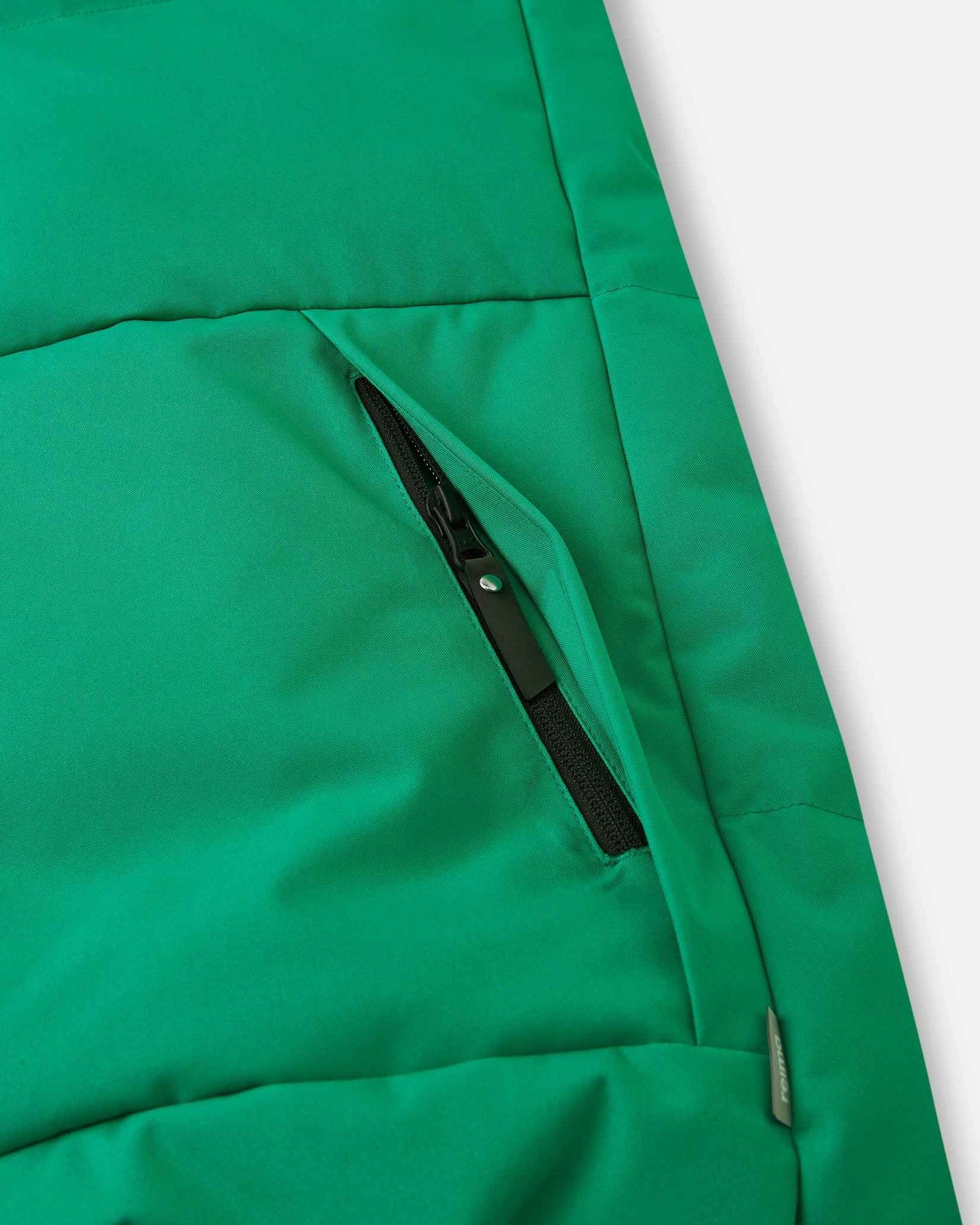 Close-up detail of the secure, hidden front zippered pocket on the quilted green body of the Reima Ranua kids' down ski jacket, perfect for safely storing small items.