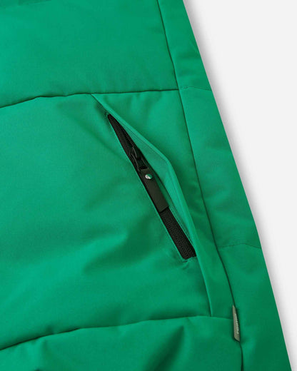 Close-up detail of the secure, hidden front zippered pocket on the quilted green body of the Reima Ranua kids' down ski jacket, perfect for safely storing small items.